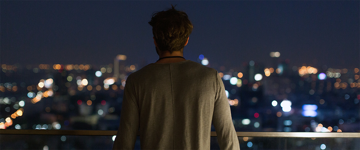 Ein Mann blickt im Dunklen auf die hellen Lichter einer Stadt.