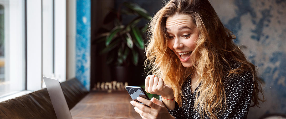 Eine Frau schaut auf ihr Handy und freut sich über etwas.